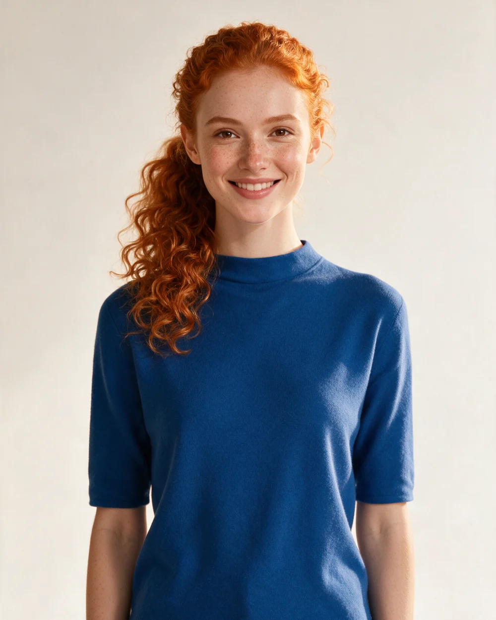 Orla O., a Fotyra spokesmodel with copper curls and freckles, smiling in a blue top in her roster portrait